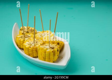 Mais, ein Snack aus reifem Mais und garniert mit Chilischoten und Honig in einem weißen schönen Geschirr, das auf einem festen Eis platziert ist angeordnet Stockfoto