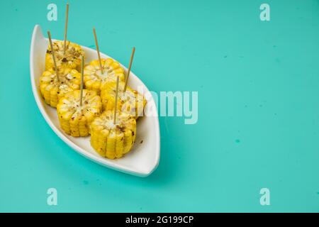 Mais, ein Snack aus reifem Mais und garniert mit Chilischoten und Honig in einem weißen schönen Geschirr, das auf einem festen Eis platziert ist angeordnet Stockfoto