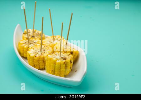 Mais, ein Snack aus reifem Mais und garniert mit Chilischoten und Honig in einem weißen schönen Geschirr, das auf einem festen Eis platziert ist angeordnet Stockfoto