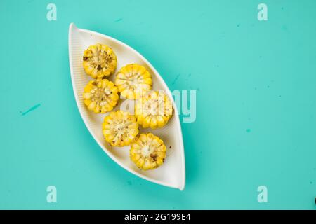 Mais, ein Snack aus reifem Mais und garniert mit Chilischoten und Honig in einem weißen schönen Geschirr, das auf einem festen Eis platziert ist angeordnet Stockfoto