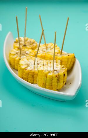 Mais, ein Snack aus reifem Mais und garniert mit Chilischoten und Honig in einem weißen schönen Geschirr, das auf einem festen Eis platziert ist angeordnet Stockfoto