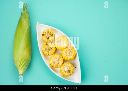 Mais, ein Snack aus reifem Mais und garniert mit Chilischoten und Honig in einem weißen schönen Geschirr, das auf einem festen Eis platziert ist angeordnet Stockfoto