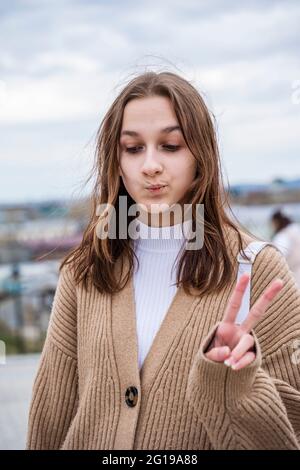 Nettes Mädchen Teenager, Schulmädchen feiert einen Sieg. Zeigt das Siegeszeichen mit den Fingern. Stockfoto