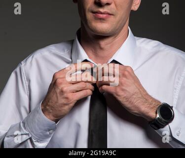 Ein Mann in einem weißen Hemd zieht eine Krawatte an, wenn er zur Arbeit oder zu einer Gala, einer Hochzeit, geht. Stockfoto