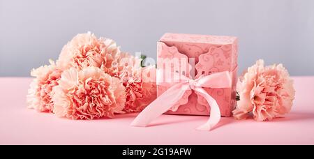 Bouquet von rosa Nelken und rosa Geschenkbox. Design Konzept der Feiertagsgrüße mit Nelkenstrauß auf rosa Hintergrund. Stockfoto