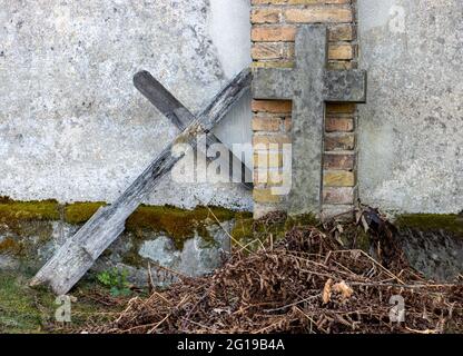 Ein altes Kreuz, das sich auf einem Friedhof an einer Mauer lehnt Stockfoto