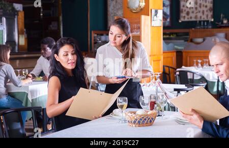 Lächelnde Kellnerin, die von einem erwachsenen Mann und einer Frau im Restaurant bestellt wurde Stockfoto