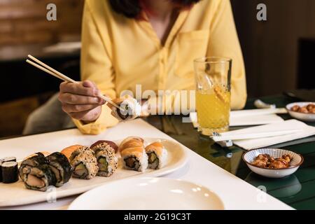 Sushi, japanische Küche, Nahaufnahme mit Frauenhand in einem Restaurant. Lifestyle Sashimi leckere Meeresfrüchte und Reisbrötchen. Gelbe Farbe des Jahres Stockfoto