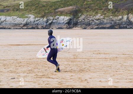 Ein Surfer mit seinem Surfbrett und läuft über Crantock Beach in Newquay in Cornwall. Stockfoto