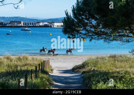 SANXENXO, SPANIEN - 19. MAI 2021: Reiter auf Pferden genießen einen sonnigen Frühlingsmorgen am Strand oder Portonovo in der Ria de Pontevedra, Spanien. Stockfoto