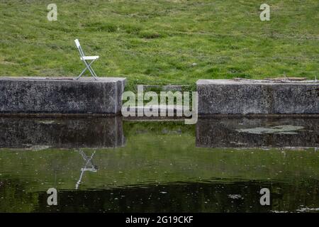 Ein einsitzender Stuhl steht am Ufer eines Wassertanks. Stockfoto