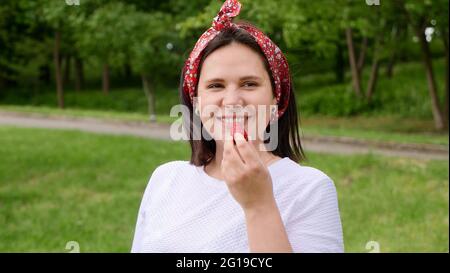 Mädchen, die Erdbeere isst, glücklich lächelt und in die Kamera schaut. Junge Frau, die rote Erdbeerbeere isst. Porträt von Mutter, Hausfrauen, Landwirt Stockfoto