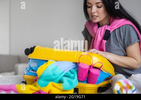 Glückliche asiatische Frau versucht, schließen gelben Koffer voller verschiedener Kleidung Accessoires und Schuhe Stockfoto