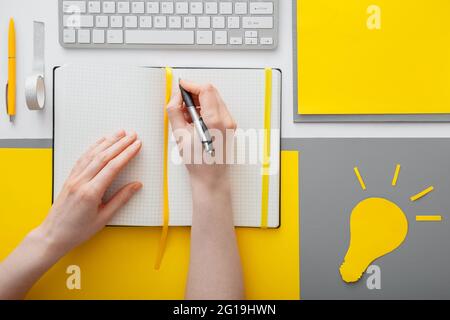 Weibliche Hände schreiben ein Ideenziel in ein leeres Notizbuch auf dem Desktop im Arbeitsbereich. Frau schreibt Liste der Ideen in Notizbuch auf grauem gelbem Hintergrund Stockfoto