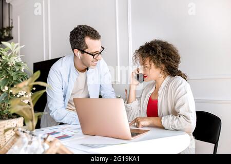 Erfolgreiche stilvolle Geschäftspartner arbeiten im modernen Büro an Projekten und diskutieren Ideen. Glückliche Kollegen, die Finanzdiagramme mit einem Laptop lernen Stockfoto