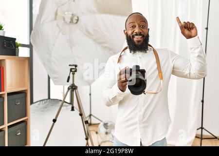 afroamerikanischer Fotograf, der im Fotostudio arbeitet, lächelt erstaunt und überrascht und zeigt mit Fingern und erhobenen Armen auf. Stockfoto