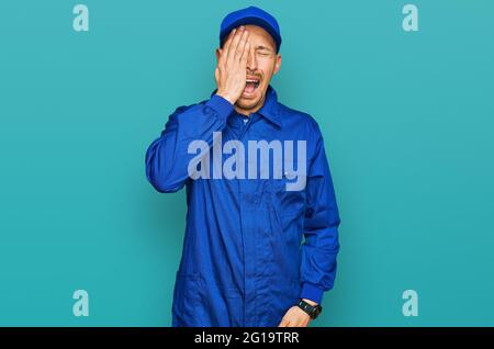 Glatze Mann mit Bart tragen Baumeister Jumpsuit Uniform gähnend müde Abdeckung halb Gesicht, Auge und Mund mit der Hand. Gesicht schmerzt bei Schmerzen. Stockfoto