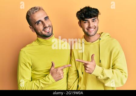 Homosexuell schwule Paar zusammen in gelben Kleidern fröhlich mit einem Lächeln Gesicht zeigt mit Hand und Finger auf die Seite mit glücklich ein Stockfoto