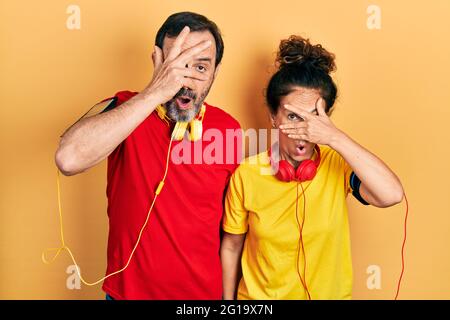 Ein Paar hispanischer Frauen und Männer mittleren Alters, die Sportkleidung und Armband tragen und mit der Hand ins Gesicht und in die Augen blicken und durch die Finger schauen Stockfoto