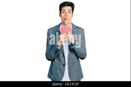 Junger hispanischer Geschäftsmann, der sein Gesicht mit Karten bedeckt, der ein Fischgesicht mit Mund und blinden Augen macht, verrückt und komisch. Stockfoto