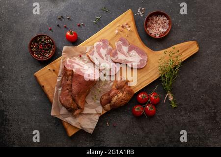 Geräuchertes Gammon in Scheiben auf einem Holzbrett mit frischen Kräutern und aromatischen Gewürzen. Naturprodukt aus biologischem Anbau, hergestellt von traditionellem ME Stockfoto