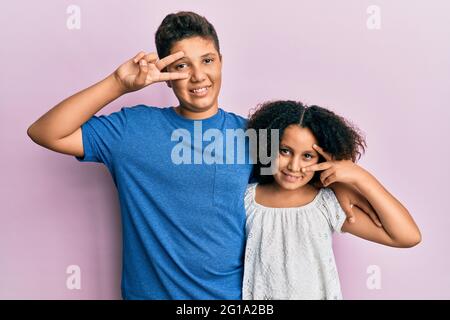 Junge hispanische Familie von Bruder und Schwester tragen legere Kleidung zusammen tun Frieden Symbol mit Fingern über dem Gesicht, lächelnd fröhlich zeigt Sieger Stockfoto