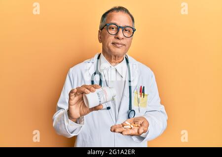 Mittelalter indischer Mann trägt Arzt Uniform hält verschreibungspflichtige Pillen entspannt mit ernster Ausdruck auf dem Gesicht. Einfach und natürlich auf die Kamera schauen Stockfoto