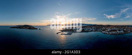 Griechenland, Koufonisia kleine Kykladen-Inseln, Luftdrohnen-Panoramablick bei Sonnenuntergang. Weiße, traditionelle Dorfgebäude, Sandstrand, Hafen und Yachthafen. Stockfoto