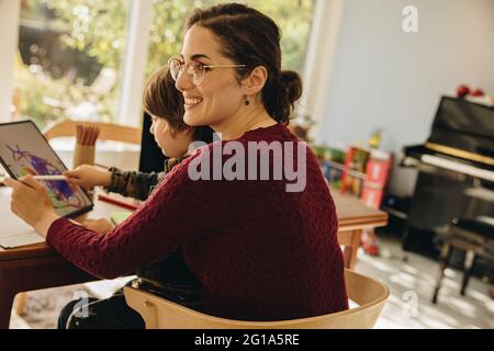Frau sitzt mit Sohn, der auf ihrem digitalen Tablet zeichnet. Mutter mit Kind, die mit einem Tablet-Computer am Tablet sitzt. Stockfoto