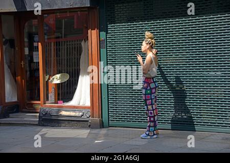 Junge Frau auf dem Handy, die sich am Grill festhält, schicke Hosen Stockfoto