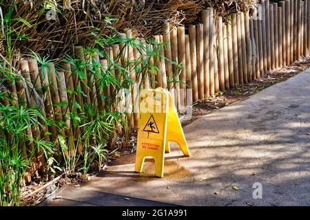 Ein Plastikwarnschild auf dem Bürgersteig bei den Holzzäunen Stockfoto