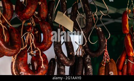 Typische spanische Würste hängen an einem Dorfstand am Lebensmittelmarkt, traditionelle Fleischprodukte Stockfoto