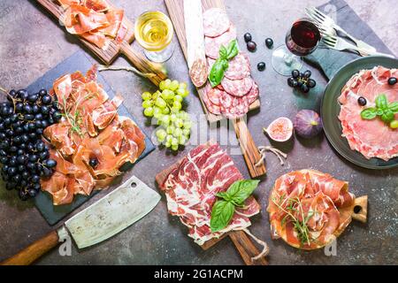 Verschiedene Arten von Jamon auf Schnittboarden mit Feigen, Trauben und Wein. Parmaschinken-Hamon auf Holzhintergrund mit Kopierraum, Draufsicht. Stockfoto