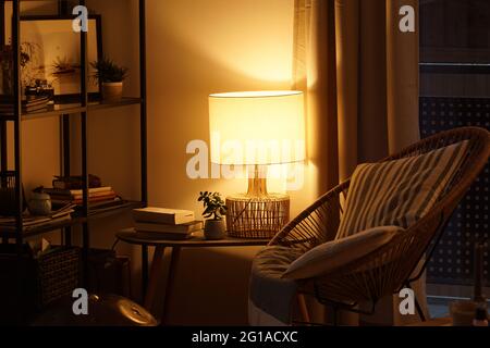 Blick auf eine gemütliche Leseecke mit einer Tischlampe, die warmes Licht ausgibt Stockfoto