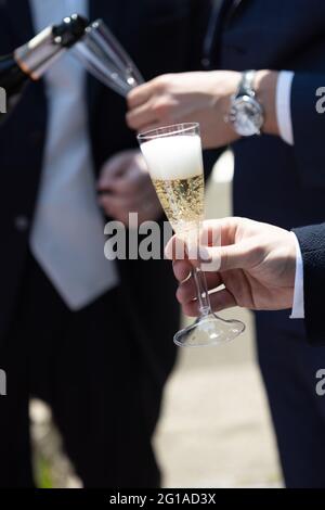 Zwei elegante Männer im Anzug, die Sekt in ein Kunststoffflötenweinglas gießen Stockfoto