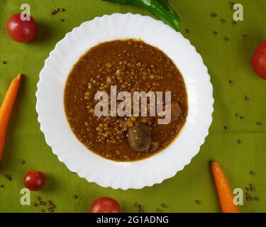 Hausgemachte Linsensuppe mit Schweinefleisch-Würstchen namens Chorizo und Blutwurst namens Morcilla in einem Gericht, das mit Gemüse auf einer Tischdecke dekoriert ist. Draufsicht Stockfoto