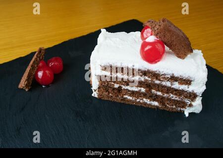 Schwarze Waldscheibe, verziert mit Kirschen und kleinen Kuchenstücken auf einem schwarzen Schieferbrett Stockfoto