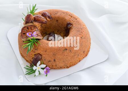 Datteln Kuchen und Dekorieren mit getrockneten Datteln. Getrocknete Quitten und Rosmarinblätter auf weißem Stoffhintergrund, gesundes Kuchenkonzept Stockfoto