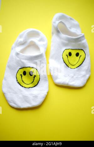 Zwei weiße Socken mit einem Smiley-Gesicht auf einem leuchtend gelben Tisch. Stockfoto