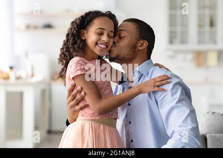 Liebevoller afroamerikanischer Mann küsst seine glückliche kleine Tochter Stockfoto