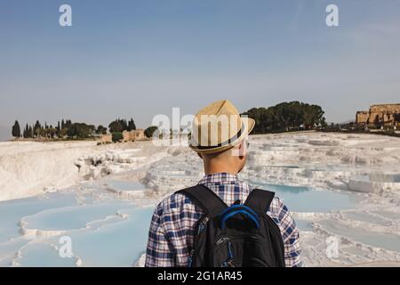 Junger männlicher Tourist in Strohhut, der auf die natürlichen Travertin-Pools schaut Stockfoto