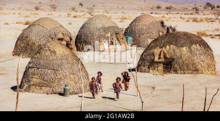 Kinder aus Baloch spielen neben ihren traditionellen Häusern im Kreis Nikshahr, Sistan und in der Provinz Baluchestan, Iran. Stockfoto