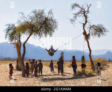 Baloch-Kinder (Baluch) spielen neben ihren traditionellen Häusern im Kreis Nikshahr, Sistan und der Provinz Baluchestan, Iran. Stockfoto