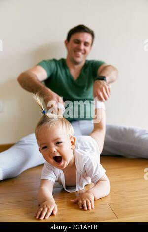 Lachende kleine Mädchen kriecht, während Papa an ihren Beinen zieht Stockfoto