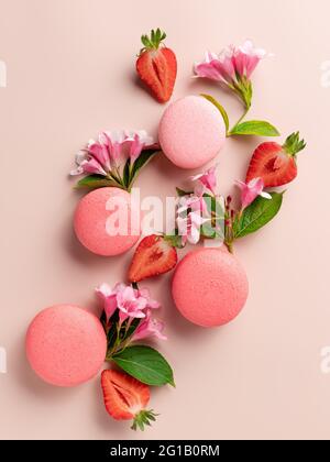 Makronen, Erdbeeren, Blumen auf beigem Hintergrund Stockfoto