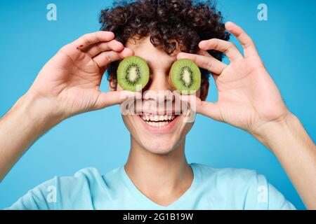 Mann mit lockigem Haar, der Kiwi in der Nähe des Klassengesichts hält Emotionen Stockfoto