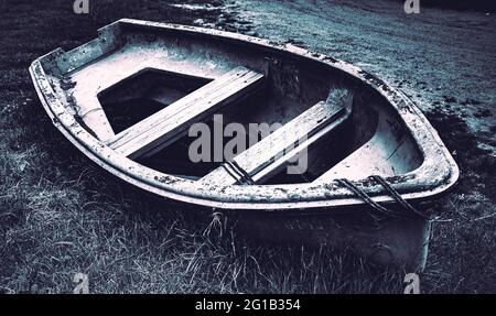 Schiffswrack - vergessenes, altes Boot liegt auf einer Wiese am Wegesrand und wird vom Wetter angegriffen - dunkle Stimmung. Stockfoto