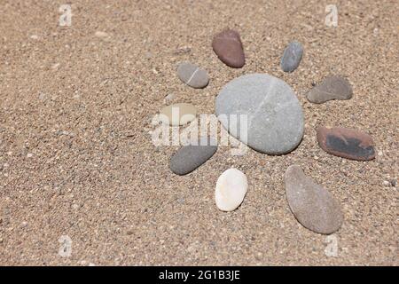Die Figur der Sonne besteht aus Steinen auf dem Strandsand Stockfoto
