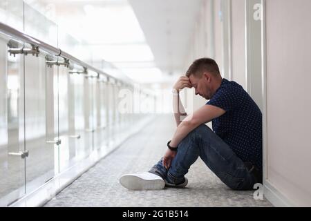 Frustrierter, müder Mann sitzt im Flur unter der Tür Stockfoto