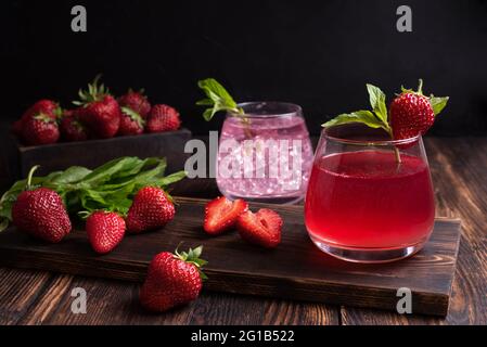 Fruchtwasser, Erdbeerlimonade mit Minzzweig mit Erdbeeren auf Holzgrund, sommerliches Erfrischungsgetränkkonzept, Nahaufnahme. Stockfoto